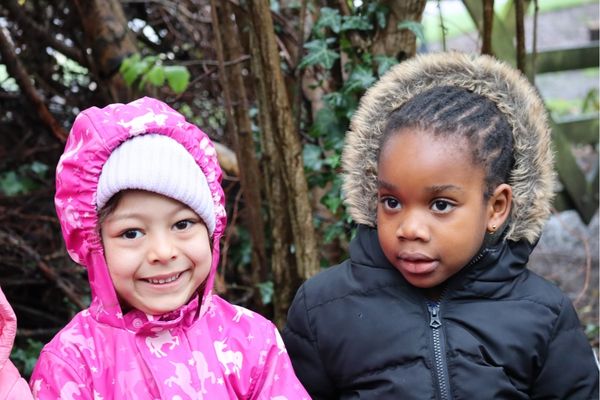 two children smiling with coats on sitting outdoors.jpg