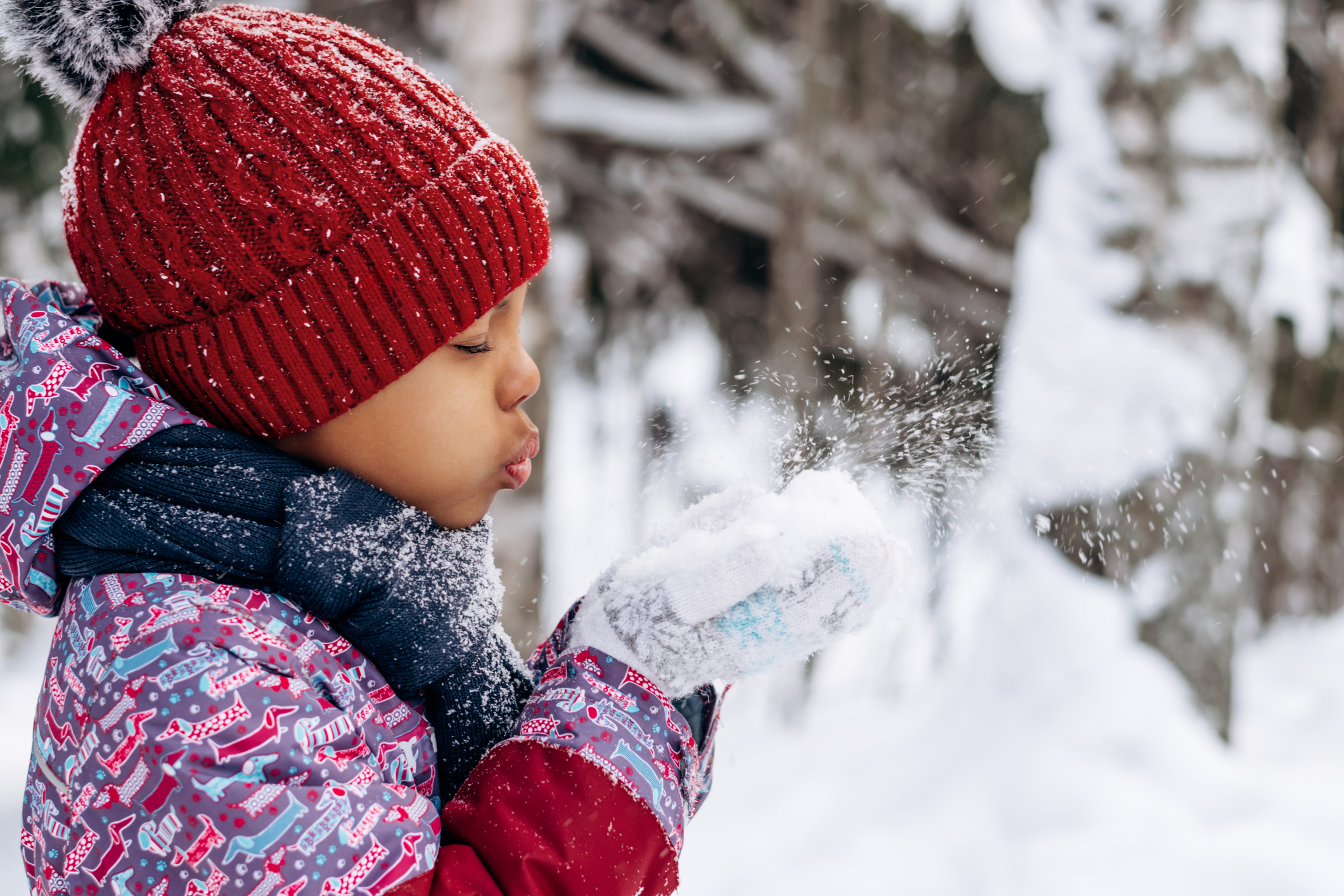 a child in winter blowing snow off their hands