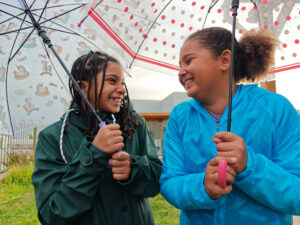 two girls smiling under umbrellas